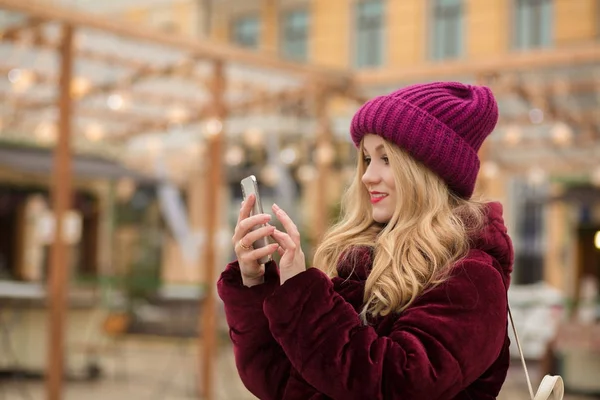 Όμορφη ξανθιά γυναίκα πληκτρολογώντας ένα μήνυμα σε ένα κινητό τηλέφωνο, στέκεται — Φωτογραφία Αρχείου