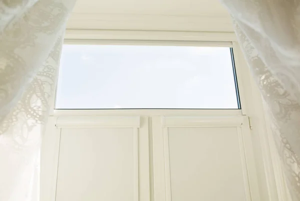 Window in a light room with the transparent tulle and closed rol