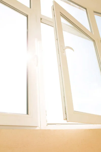 Открытое PVC окно с яркой вспышкой солнца на фоне многоэтажки — стоковое фото