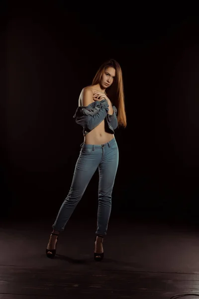 Slim young woman in trendy jeans apparel posing in the dark — Stock Photo, Image