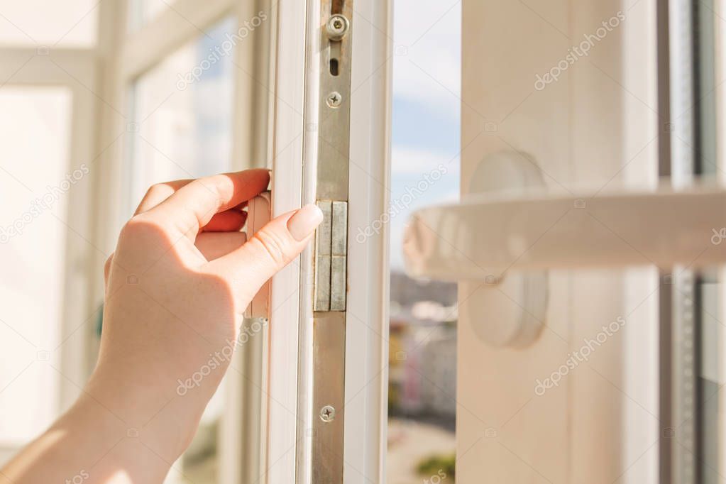 Woman's hand opening pvc window on the background of high-rise b