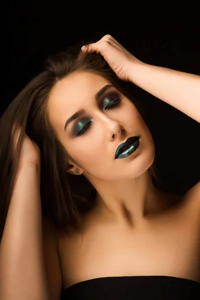 Glamorous brunette lady with art metallic green makeup posing wi