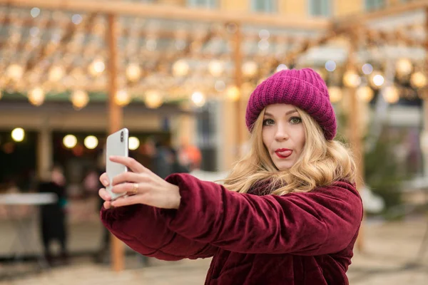 Divertente donna bionda vestita con vestiti caldi facendo selfie al — Foto Stock