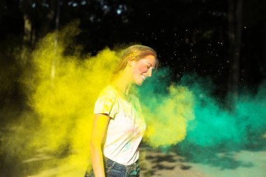 Sarı ve yeşil kuru boya ile Holi oynayan neşeli sarışın kadın
