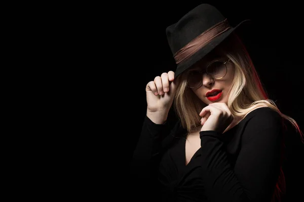 Luxuriöse junge Frau trägt schwarze Bluse, Hut und Brille, pos — Stockfoto