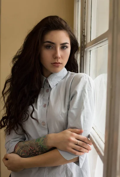 Υπέροχη νεαρή γυναίκα με σγουρά μαλλιά και ένα τατουάζ σε pos βραχίονα της — Φωτογραφία Αρχείου