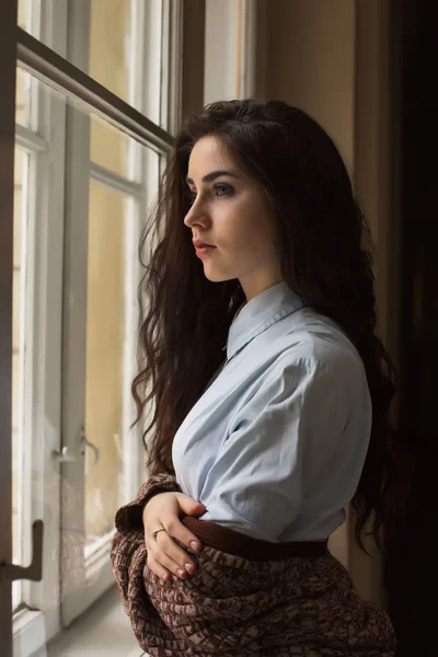 Wanita muda cantik dengan rambut keriting berpose di dekat jendela — Stok Foto