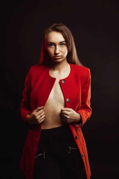 Спокуслива молода жінка в модному червоному пальто, одягненому на оголеному бої — стокове фото