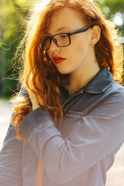 Tierna mujer joven pelirroja en jeans camisa y gafas posando —  Fotos de Stock