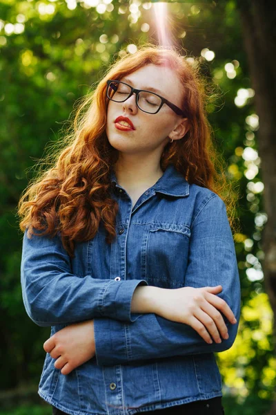 Atraente menina de cabelos vermelhos em óculos posando em raios de sol — Fotografia de Stock