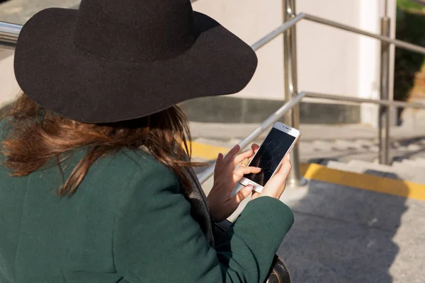 Стильна одягнена молода жінка, друкуючи смс на смартфоні з б — стокове фото