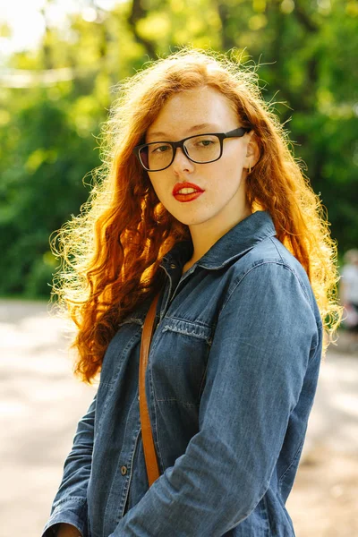 Menina de cabelos vermelhos atraentes em camisa jeans e óculos posando em — Fotografia de Stock