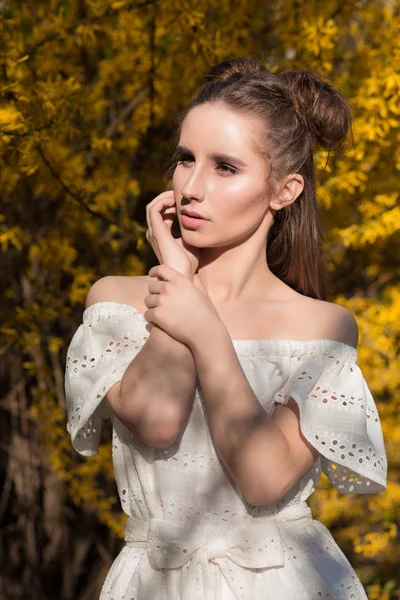 Chica morena de moda posando cerca del árbol floreciente en blanco — Foto de Stock