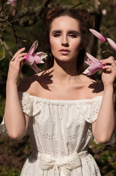 Chica morena de moda posando cerca del árbol de magnolia floreciente — Foto de Stock