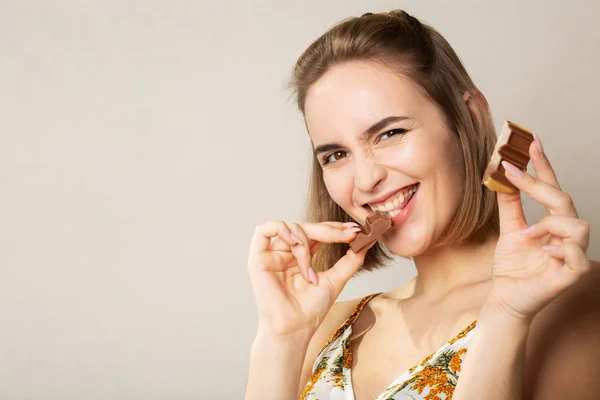 Vrij vrolijke vrouw eet melk chocolade poseren op een grijze studi — Stockfoto