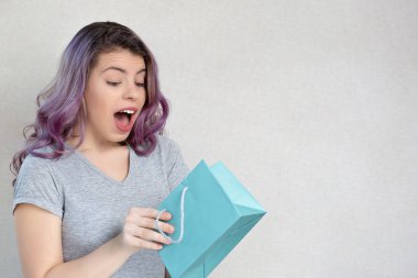 Neşeli kız gri bir arka planda hediyesini tutuyor.