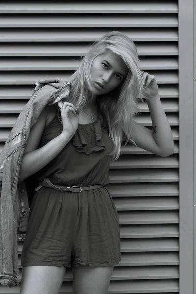 时尚金发女人穿着休闲装站在金属百叶窗前拍的街头照片 — 图库照片