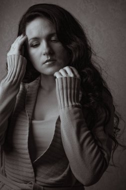 Uzun kıvırcık saçlı üzgün genç kadın gölgede örülmüş bir ceket giyiyor. Tek renkli tonlama