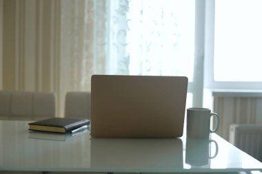 Dizüstü bilgisayar, günlük ve pencerenin yanındaki mutfak masasında bir fincan çay. Karantina sırasında evden çalışmak