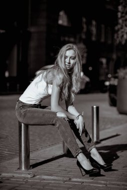 Günlük yırtık kot pantolon ve tişört giyen, çitlerde poz veren seksi genç bir kadın. Tek renkli tonlama