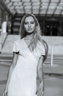 Güzel, uzun saçlı, güzel vücutlu bir kadın, güneşli bir sokakta poz veriyor. Monokrom rengi