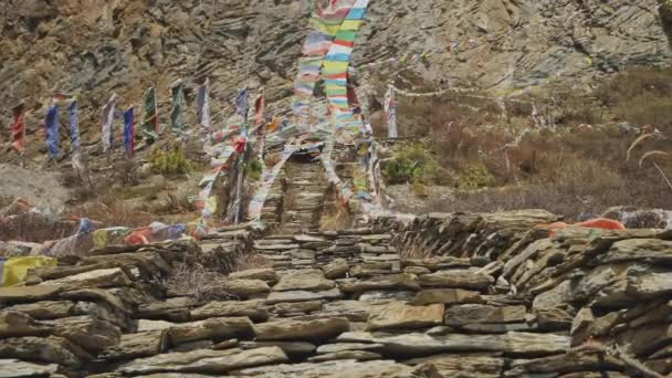 Coloured prayer flags flapping above stone stairs to Milarepa cave, Nepal — Stock Video