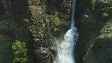 Şelale akıntısı kayalık uçurumdan aşağı akıyor, etrafa sıçrıyor.