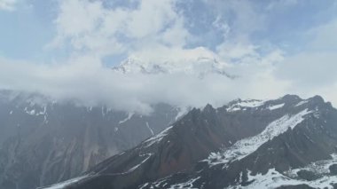 Keskin kar kayalarının yanında uç, gökyüzü yüksekliğinde Annapurna dağları bulutların üstünde, Nepal 