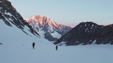 Turistler geniş kar yamaçlarında yükselirler, şafak vakti dağlarda yürüyüş yaparlar.