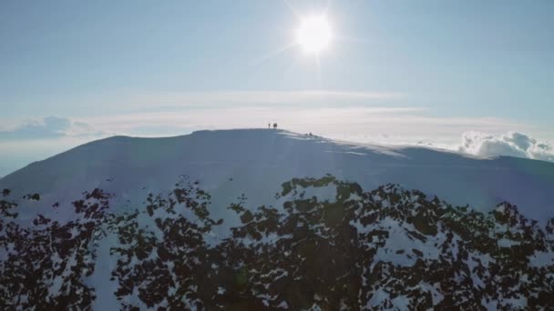Αλπινιστές σε μια χιονισμένη βουνοκορφή, ο ήλιος λάμπει πάνω από την κορυφή, ψηλά πανόραμα — Αρχείο Βίντεο