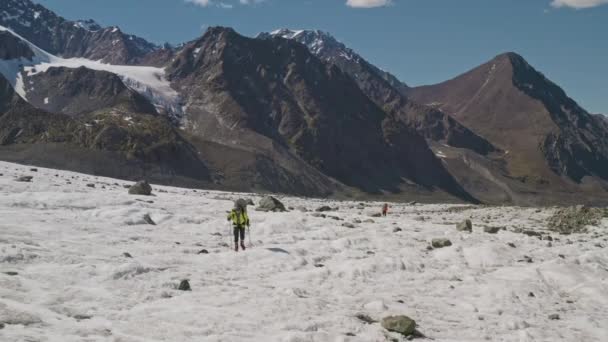 Панорама, туристы, прогуливающиеся по растопленной снежной долине с большими камнями — стоковое видео
