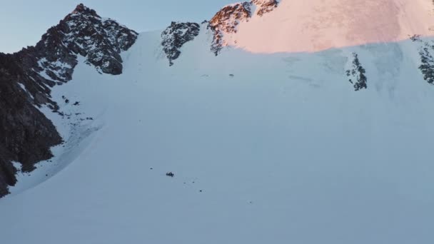Альпіністи біля підніжжя крутої снігової стіни, сходження в скелястих горах на рожевому світанку — стокове відео