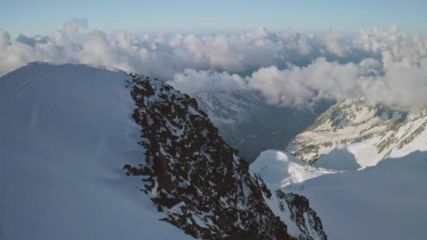 Panorama aéreo sobre la cima nevada de la montaña, nubes bajo la cumbre — Vídeos de Stock