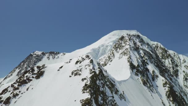 完璧な雪の白い山の頂上の周りのドローンサークルは青空の上に輝きます — ストック動画