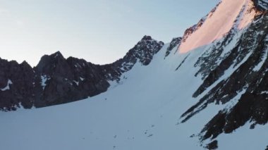 Muhteşem alp manzarası, dik donmuş kar yamacı, şafakta kayalık tepe.