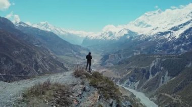 Yalnız bir adam uçurumun kenarındaki yüksek uçurumda duruyor. Derin dağ nehir geçidinde.