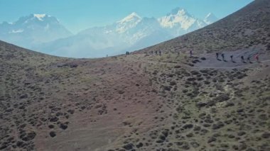 Turistler mavi sisli karlı tepelere karşı muazzam güneşli yamaçlarda yukarı doğru yürüyorlar.