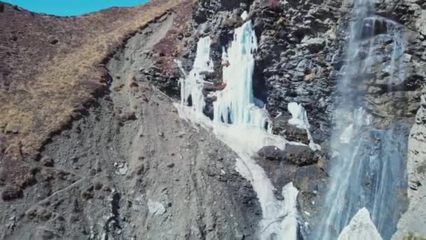 Fantastiska berg vattenfall faller från stenig scree klippa med frysta istappar — Stockvideo