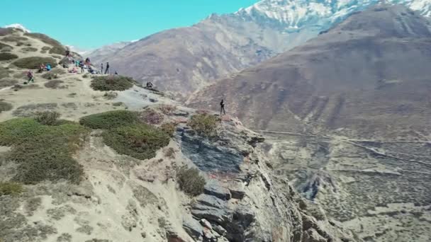 Turyści odpoczywający na skraju wysokiej skały, oszałamiająca panorama gór śniegowych wokół — Wideo stockowe
