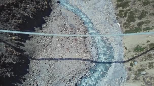 Pont suspendu suspendu au-dessus des gorges rocheuses de la rivière contre le panorama de montagne enneigé 