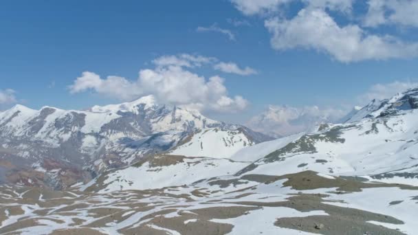Highland panorama, witte pieken raken wolken in blauwe lucht, besneeuwd patroon op de grond — Stockvideo