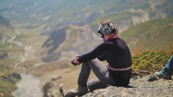 Mujer sentarse en el borde del abismo por encima de garganta profunda, disfruta con vistas a las montañas — Vídeos de Stock