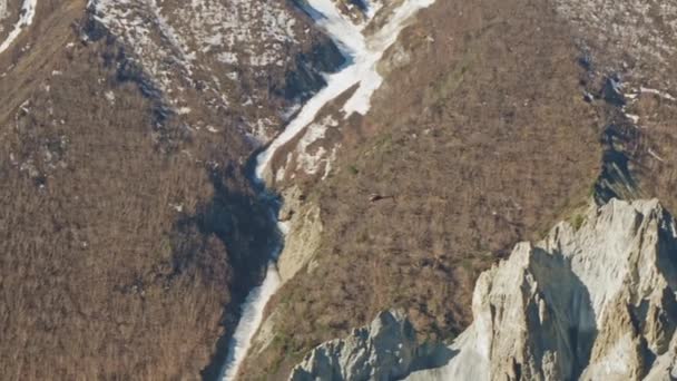 Helicóptero vuela por encima de acantilados rocosos agudos en las montañas, pendientes nevadas severas gigantes — Vídeo de stock