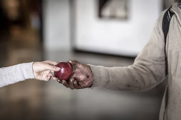 Mujer joven dando una manzana a una persona sin hogar — Foto de Stock