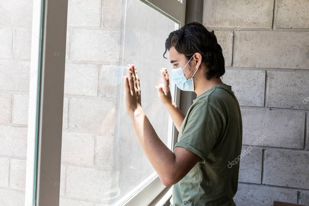 Man in quarantine with face masks looking out of their house through the window. 