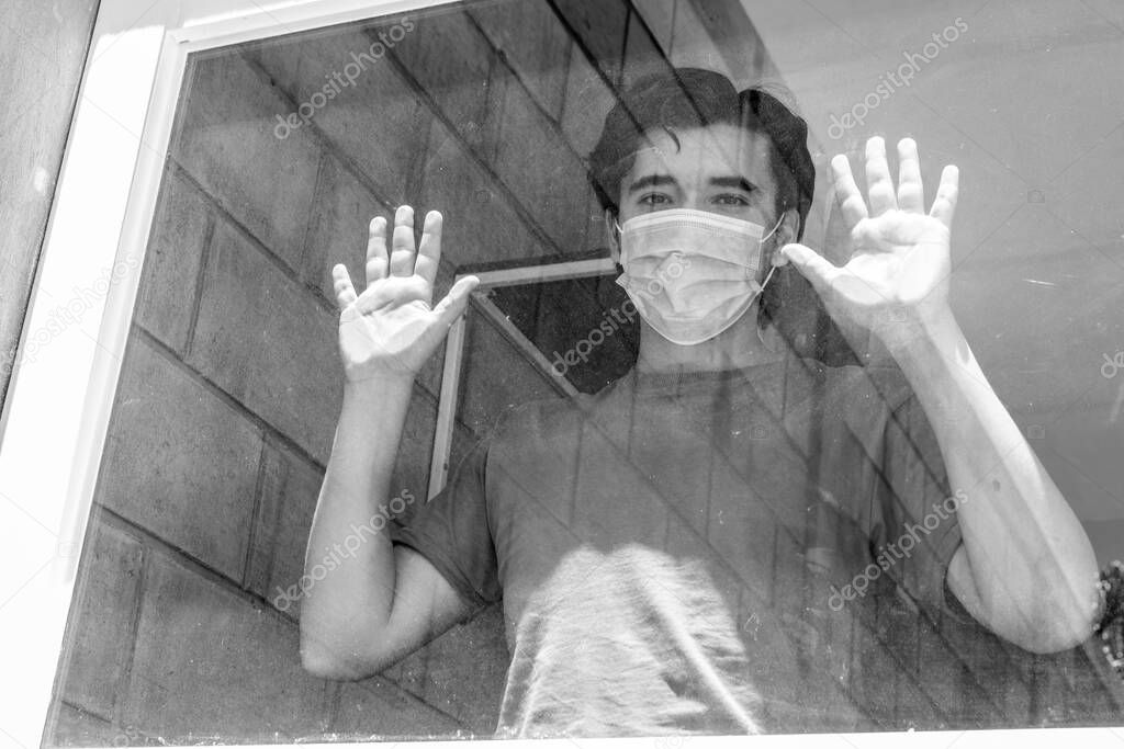 Man in quarantine with face masks looking out of their house through the window. Black and white