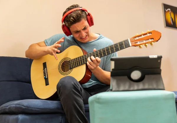 Young man in COVID-19 disease quarantine. Man taking guitar lessons online