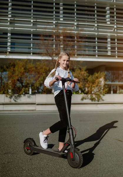 Teen girl rides an electric scooter, a cheerful girl rides a scooter at sunset