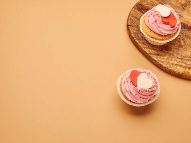 Mutfak tahtasında bej rengi kahverengi arka planda kalpleri olan pembe kekler.