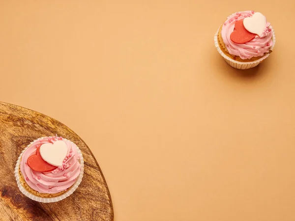 Mutfak tahtasında bej rengi kahverengi arka planda kalpleri olan pembe kekler.